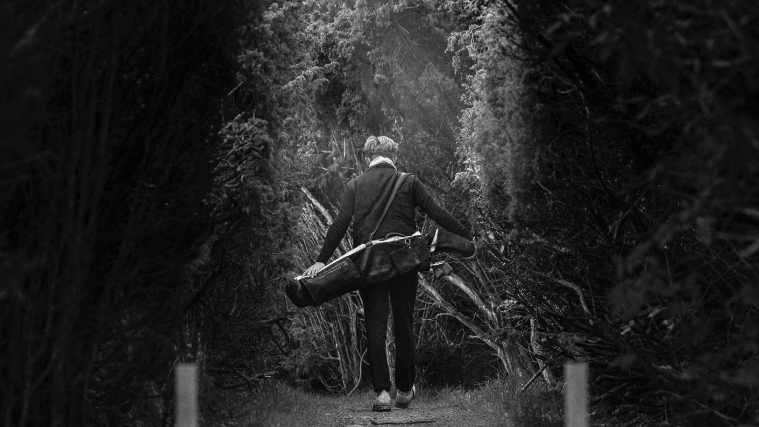 Golfer auf einem von Bäumen gesäumten Weg mit einem Pine Coast Carrybag über der Schulter